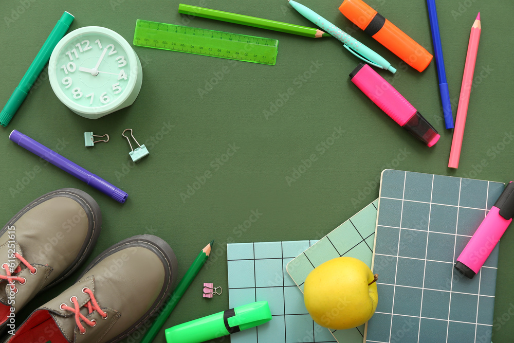 Stylish shoes with apple, alarm clock and different stationery on green background