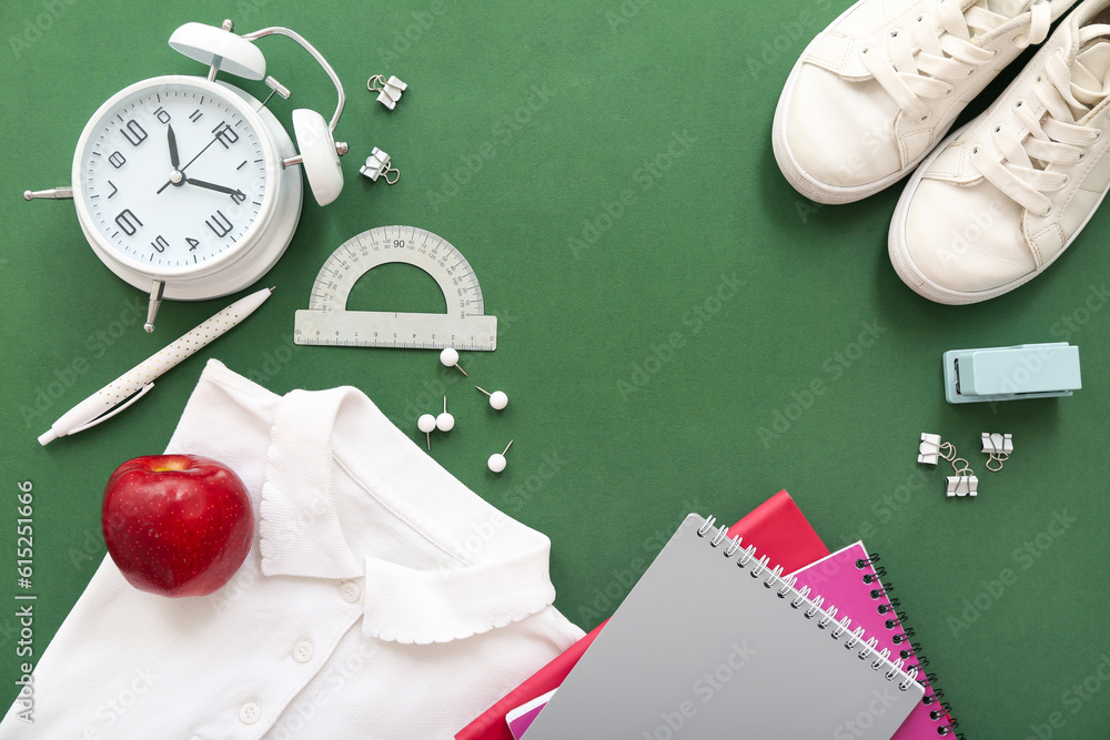 Stylish shirt with shoes, red apple and different stationery on green background