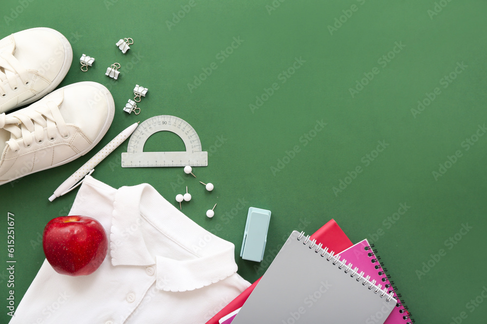 Stylish shirt with shoes, red apple and different stationery on green background