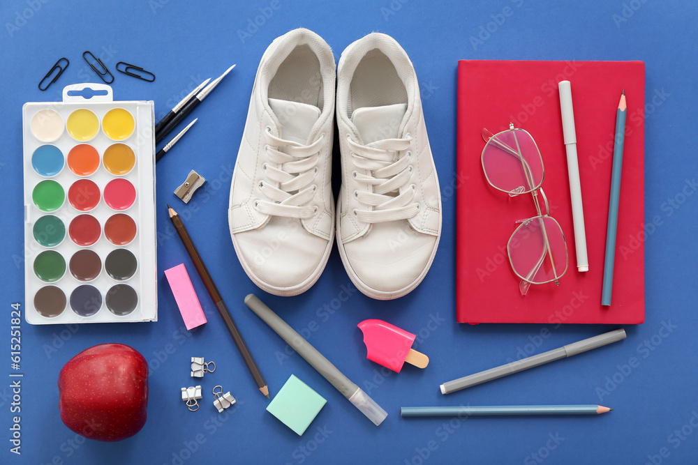 Sneakers with fresh red apple, eyeglasses and different stationery on blue background