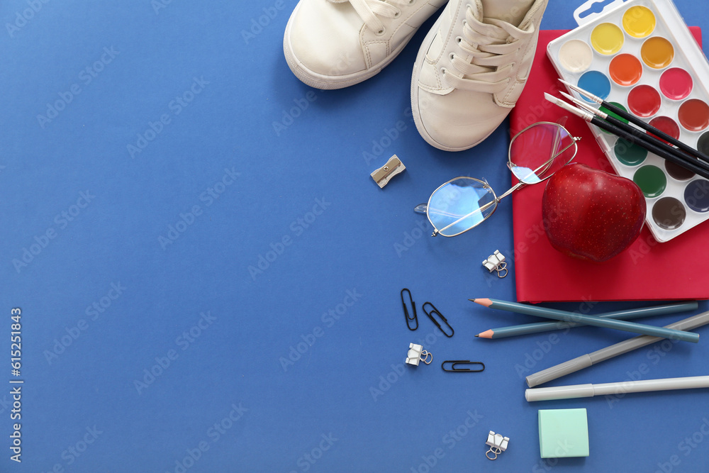 Sneakers with fresh red apple, eyeglasses and different stationery on blue background