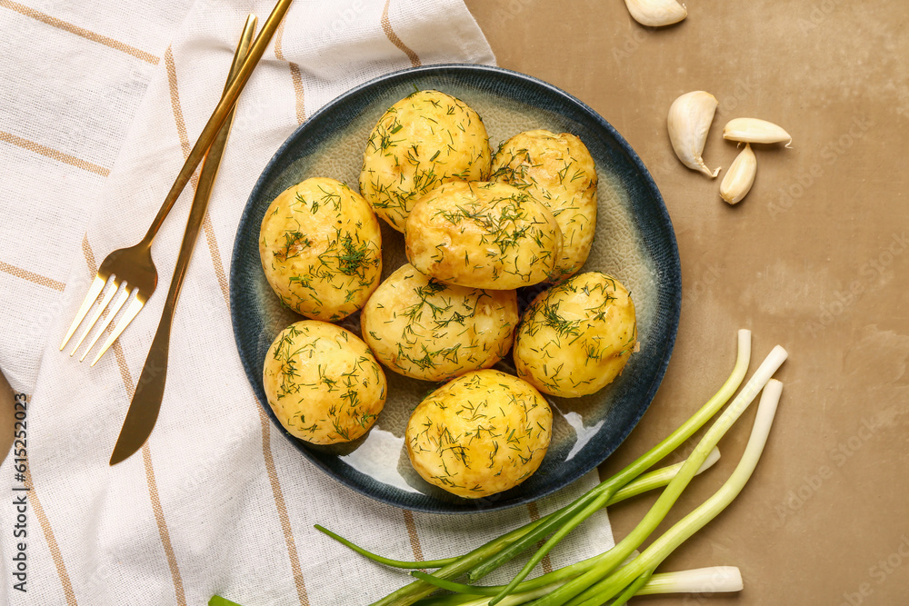 Plate of boiled baby potatoes with dill and green onion on brown background