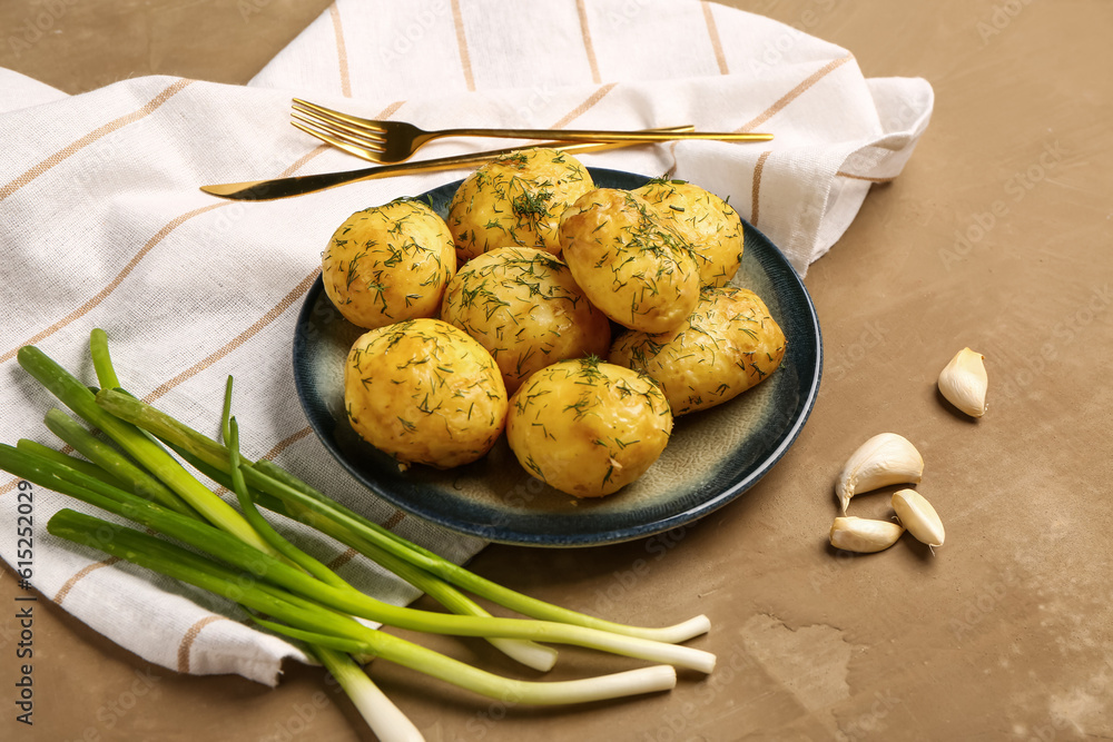 Plate of boiled baby potatoes with dill and green onion on brown background