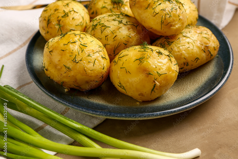 Plate of boiled baby potatoes with dill and green onion on brown background