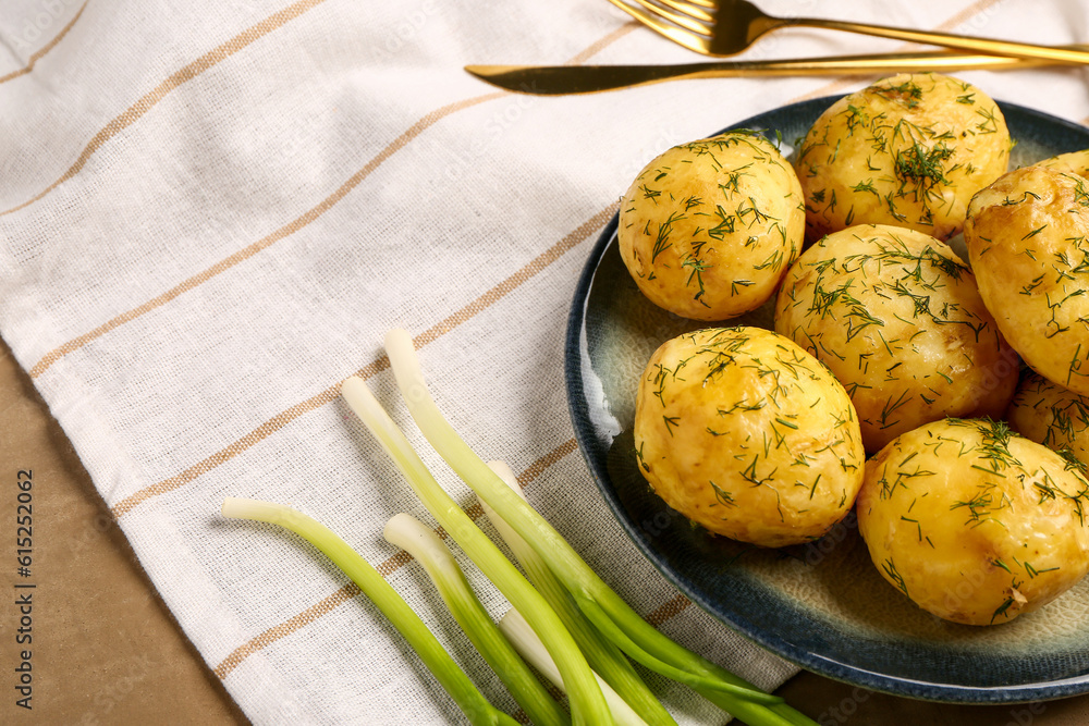 Plate of boiled baby potatoes with dill and green onion on brown background