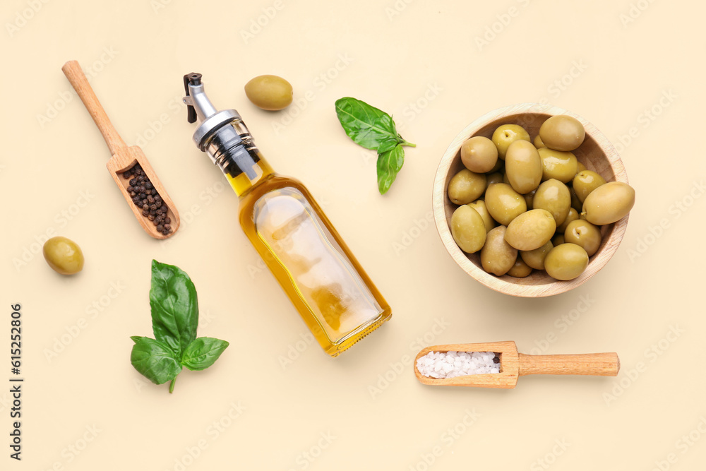 Bowl with ripe olives and bottle of oil on beige background