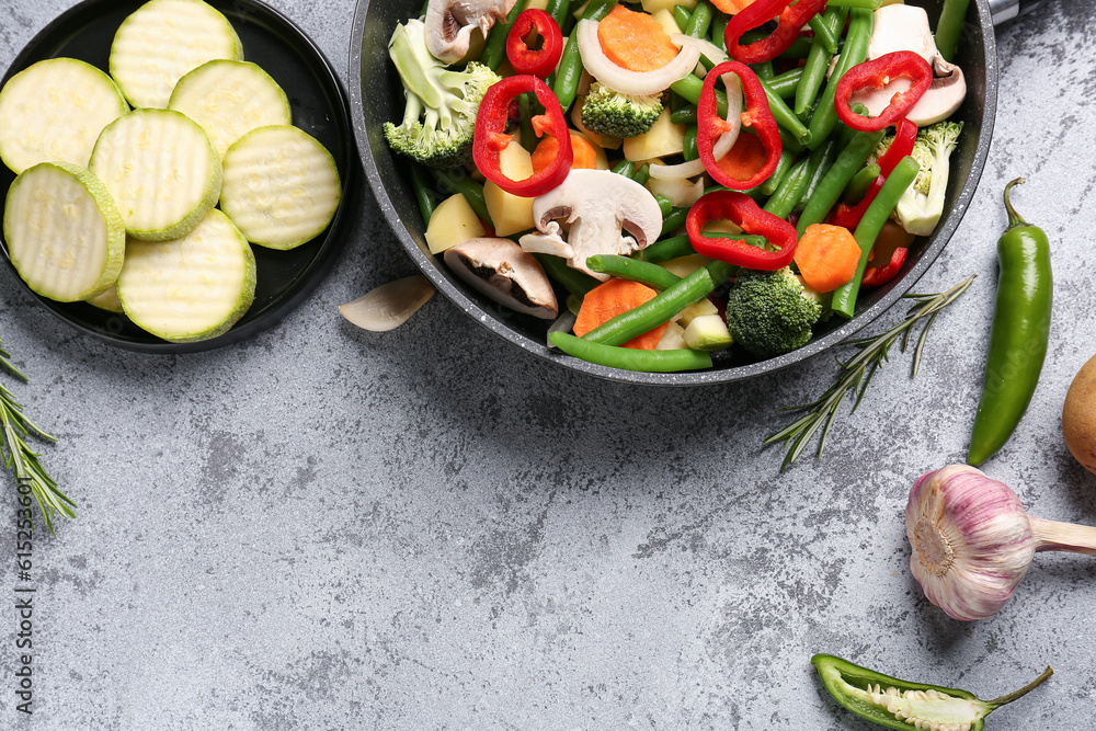 Frying pan with fresh vegetables on grey background