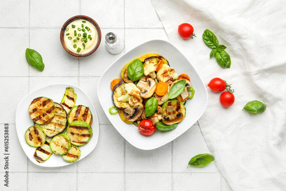 Plates with grilled vegetables and sour cream on white tile background