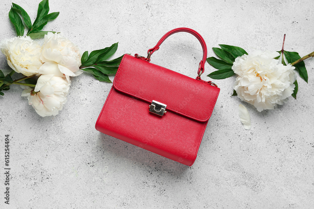 Stylish female bag and beautiful peony flowers on light background