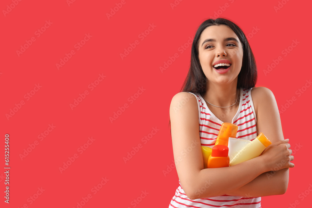 Young woman with bottles of sunscreen cream on red background