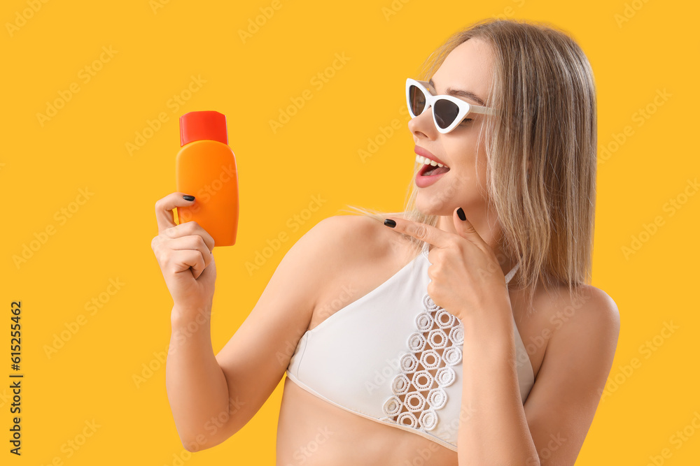 Young woman pointing at sunscreen cream on yellow background