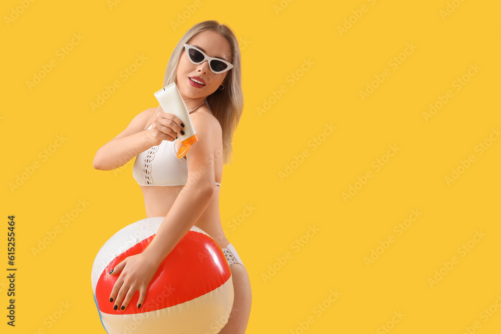 Young woman with sunscreen cream and beach ball on yellow background