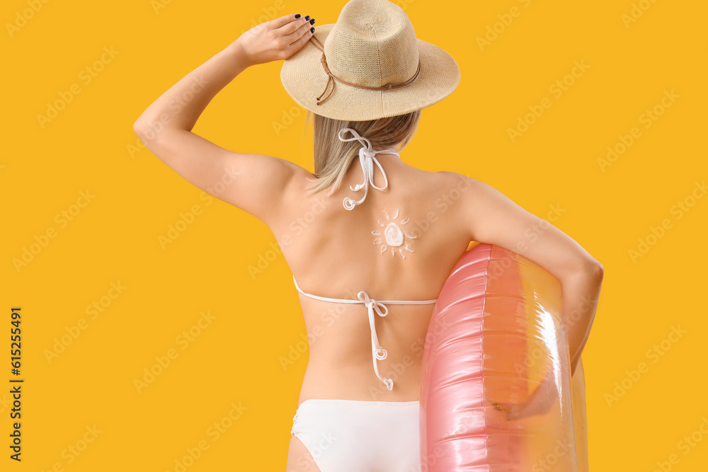 Young woman with sun made of sunscreen cream on her back and inflatable ring against yellow backgrou