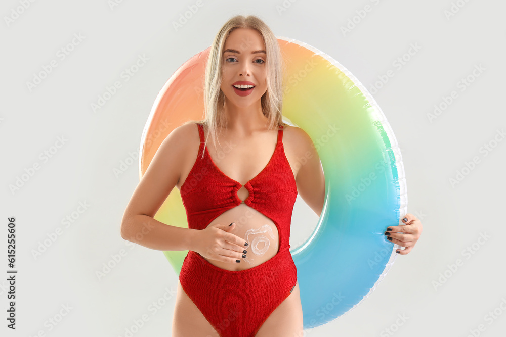 Young woman with sunscreen cream and inflatable ring on light background