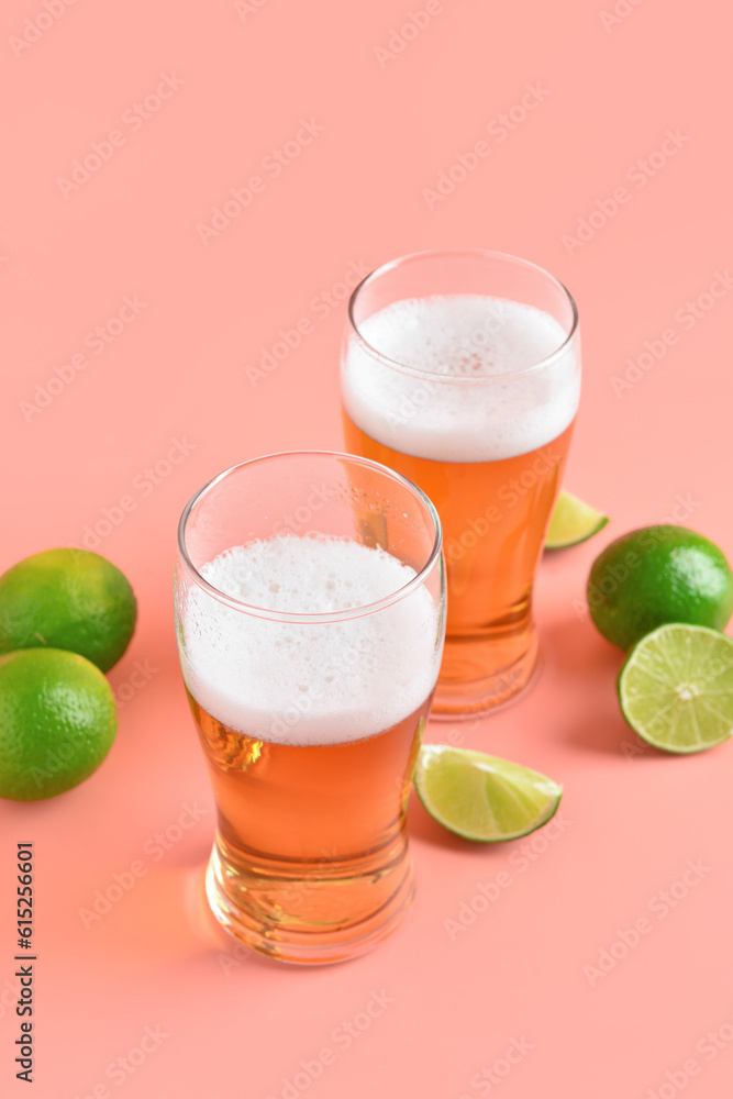 Glasses of cold beer with lime on pink background