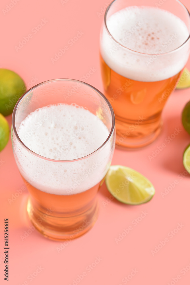 Glasses of cold beer with lime on pink background