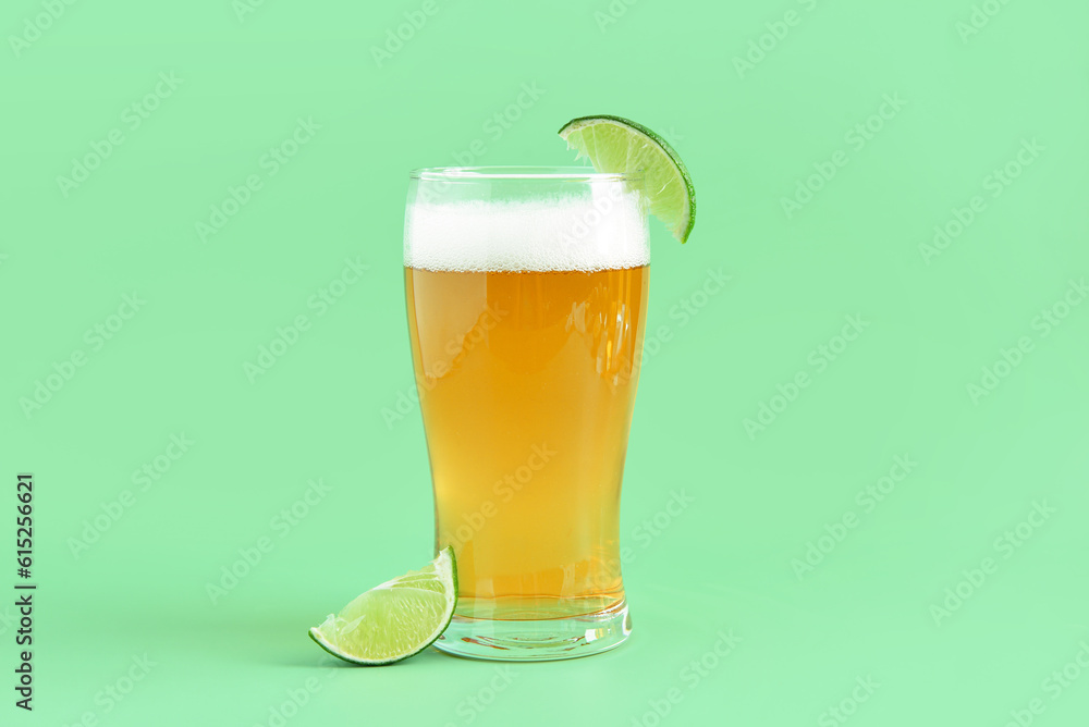 Glass of cold beer with lime on green background