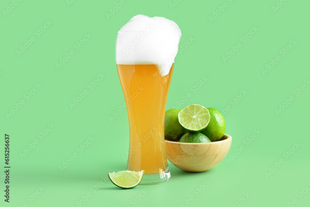 Glass of cold beer with lime on green background