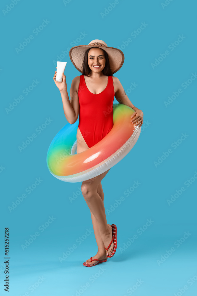 Young woman with sunscreen cream and inflatable ring on blue background