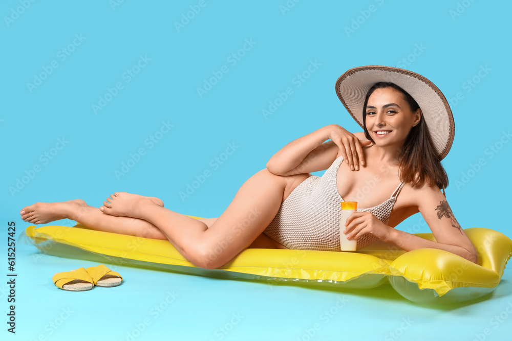 Young woman with sunscreen cream and inflatable mattress on blue background