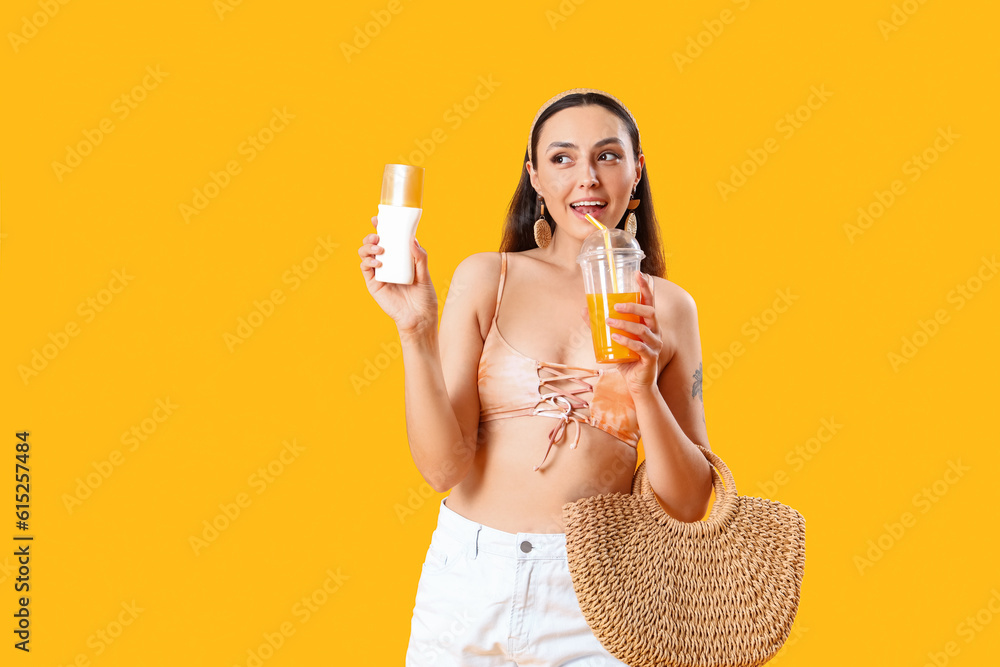 Young woman with sunscreen cream, juice and beach bag on yellow background