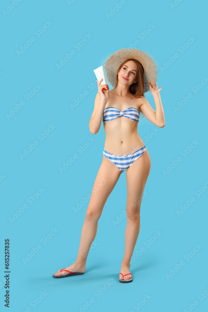 Young woman with sunscreen cream on blue background