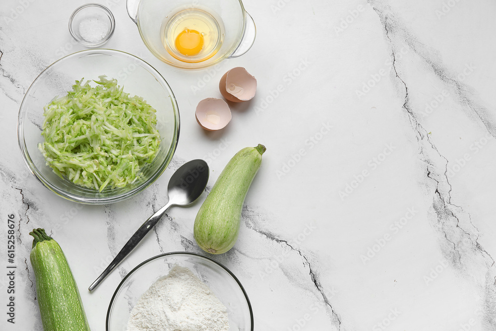 Bowls with ingredients for preparing zucchini fritters on white marble background