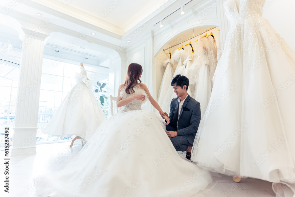 Asian beautiful bride trying on wedding gown with her fiance in studio. 