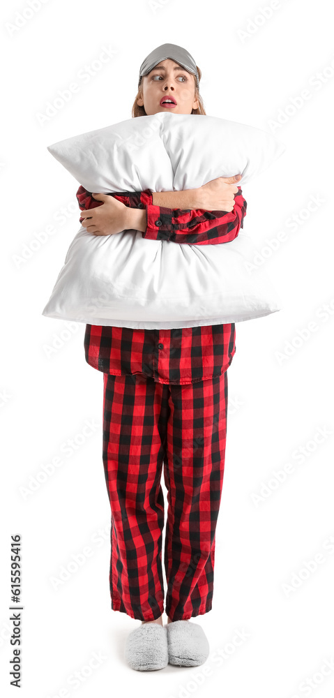 Worried young woman in checkered pajamas with pillow on white background