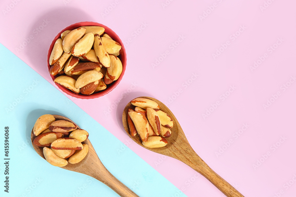 Bowl and spoons of tasty Brazil nuts on color background