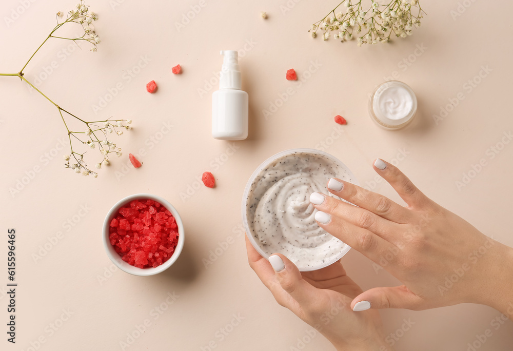 Female hands with jar of body scrub, cosmetic products, sea salt and gypsophila flowers on color bac