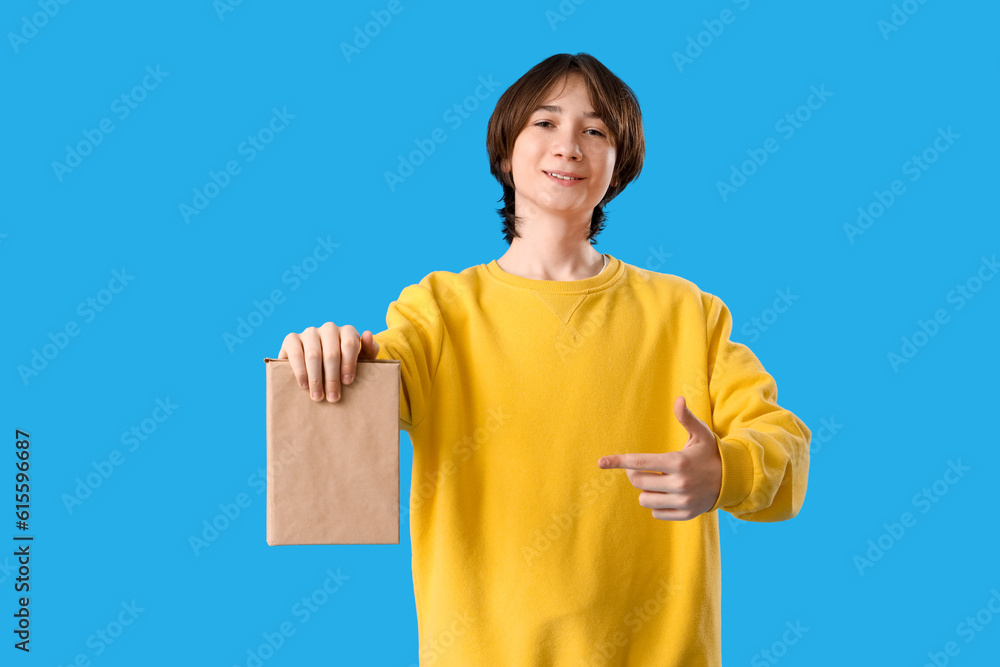 Teenage boy pointing at book on blue background