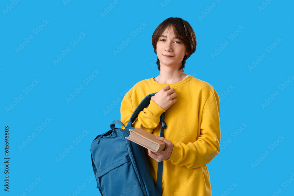 Teenage boy with book and backpack on blue background