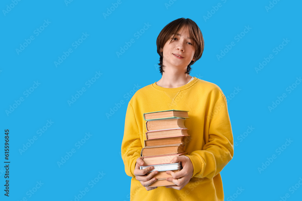 Teenage boy with stack of books on blue background