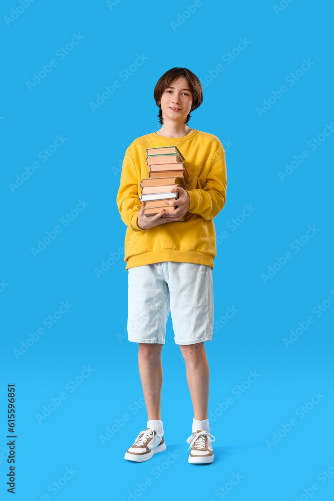 Teenage boy with stack of books on blue background