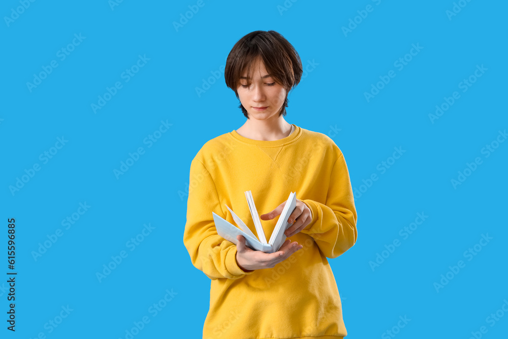 Teenage boy reading book on blue background