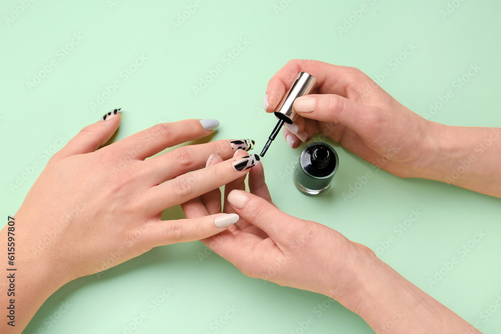 Manicure master applying polish onto press-on nail on green background, closeup