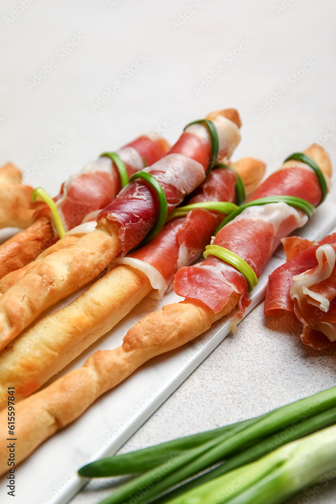 Board of tasty Italian Grissini with bacon on light background, closeup