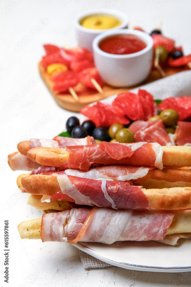 Plate of tasty Italian Grissini with bacon on light background, closeup