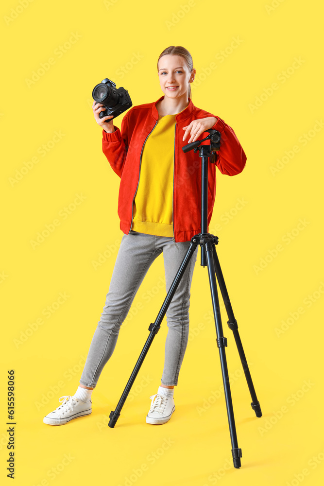 Female student with photo camera on yellow background