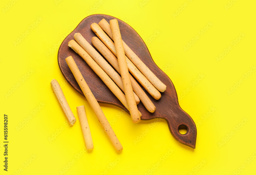 Wooden board with tasty Italian Grissini on yellow background