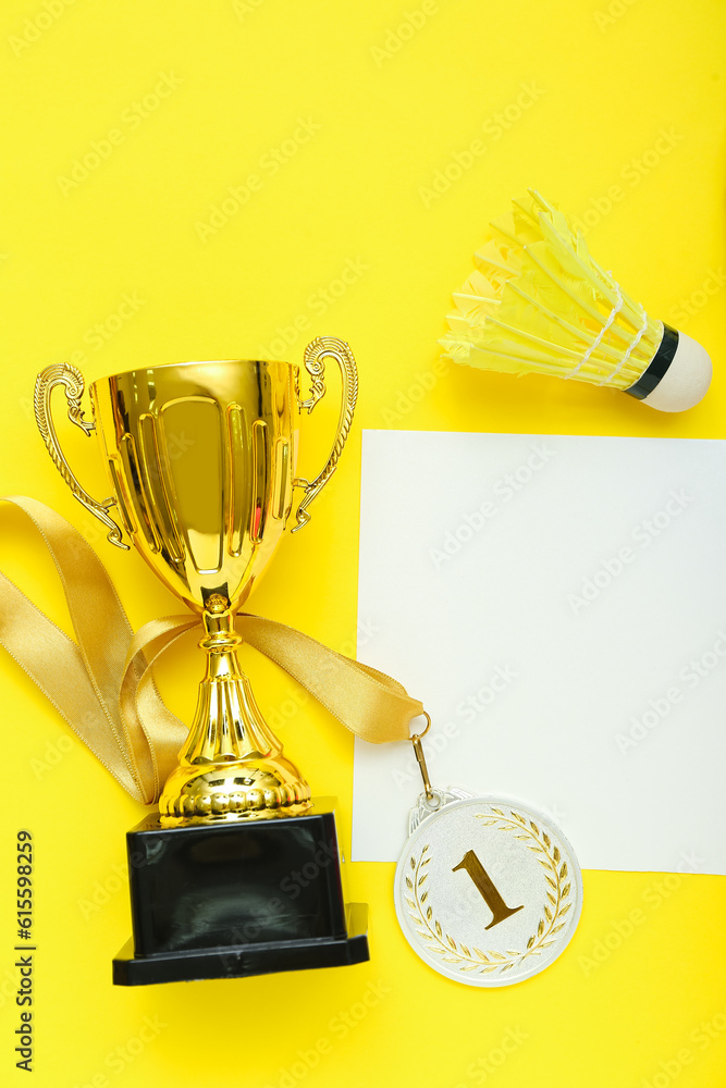 Blank card with gold cup, first place medal and badminton equipment on yellow background