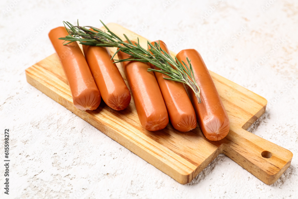 Wooden board with tasty sausages on light background