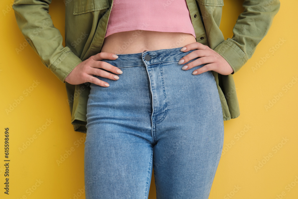 Young woman in stylish jeans on yellow background, closeup