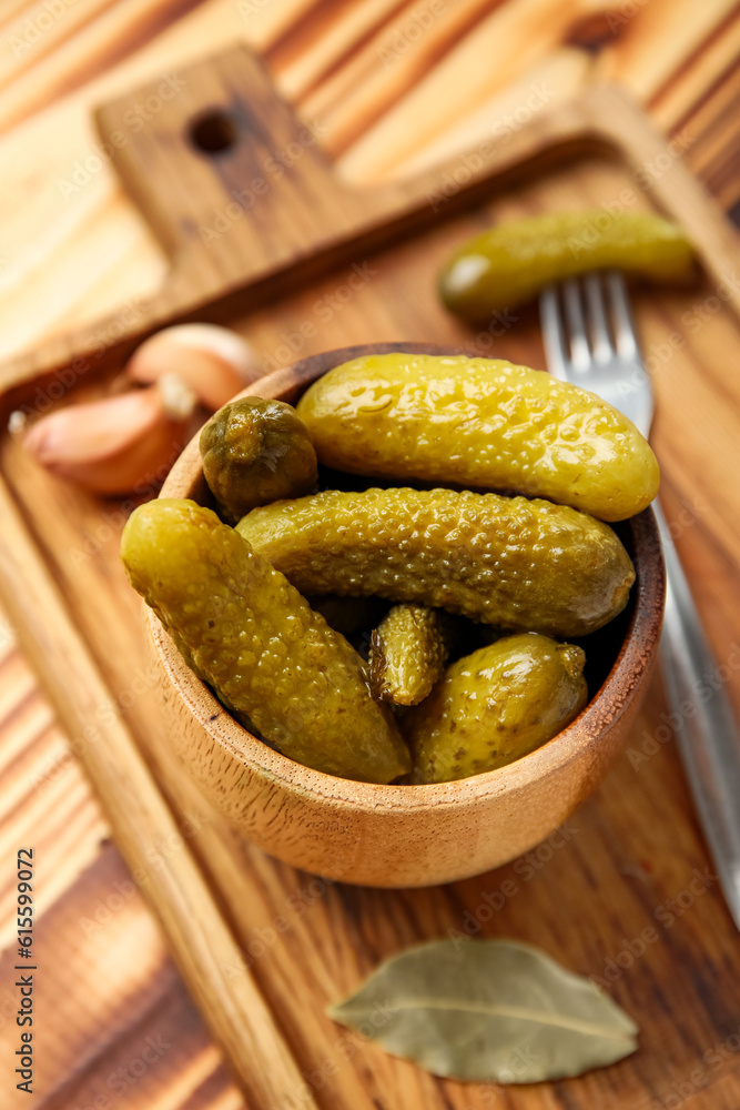 Bowl with tasty fermented cucumbers, board and ingredients on wooden background