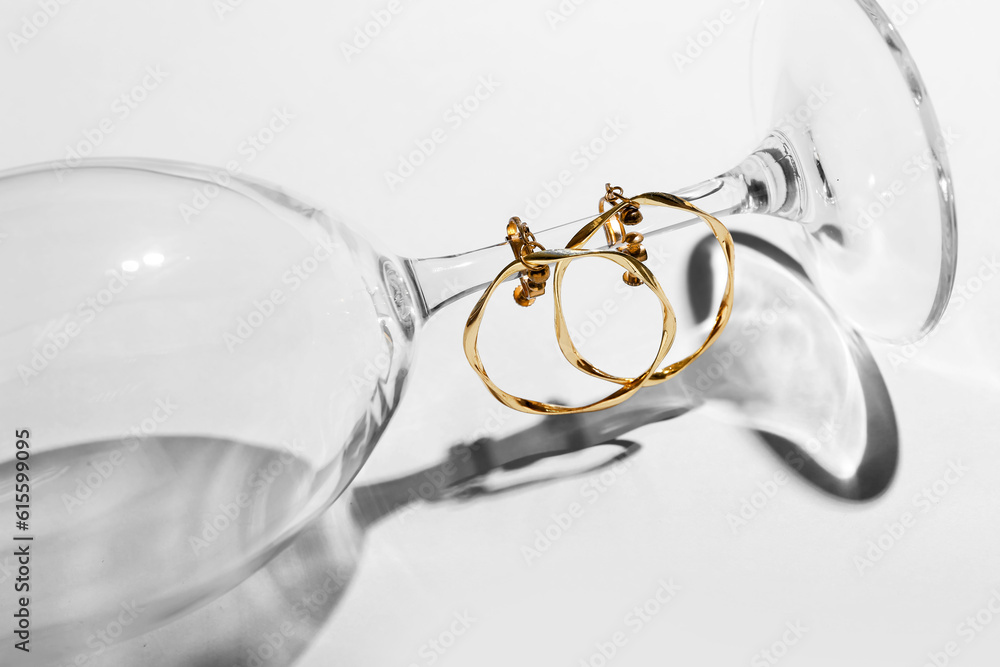 Glass with golden earrings on light background, closeup