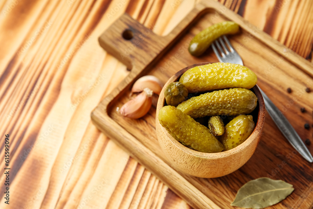 Bowl with tasty fermented cucumbers, board and ingredients on wooden background