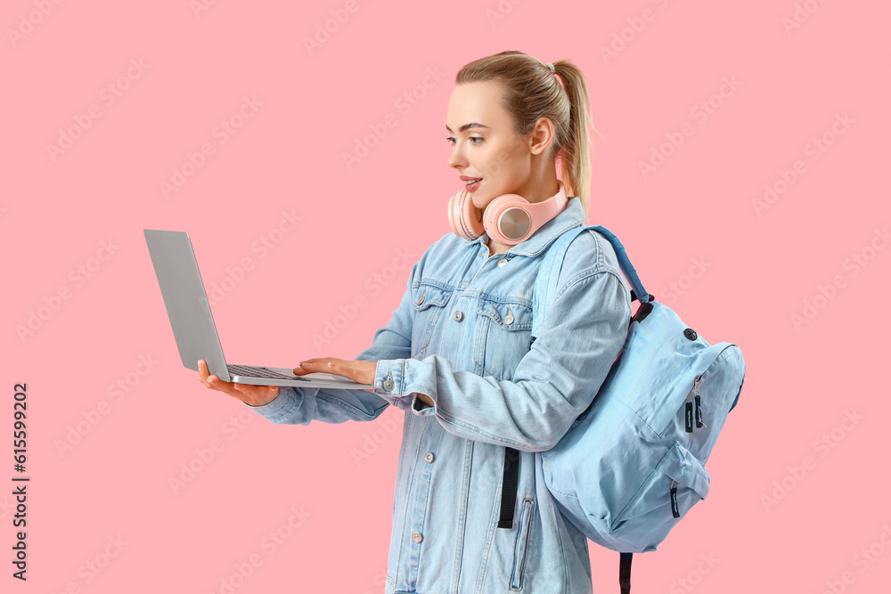 Female student using laptop on pink background