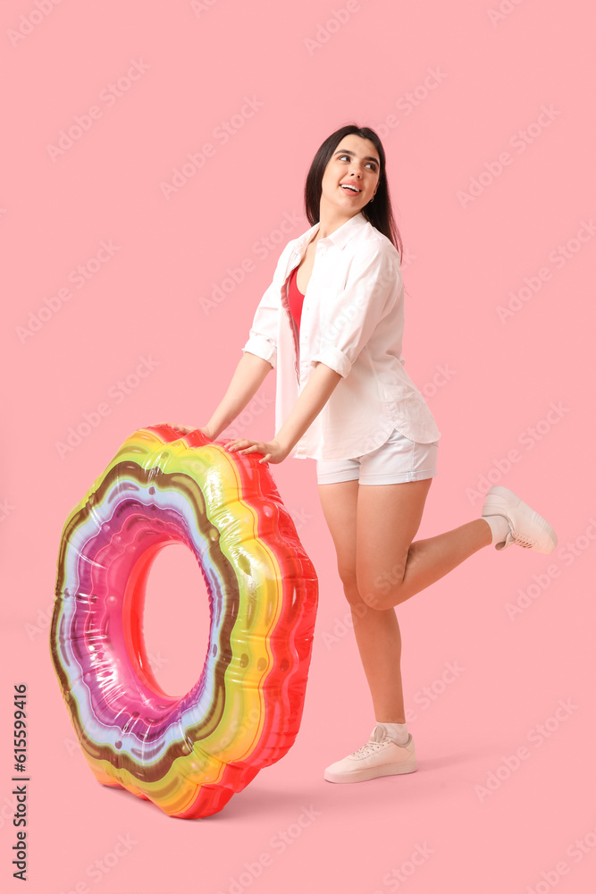 Young woman with inflatable ring on pink background