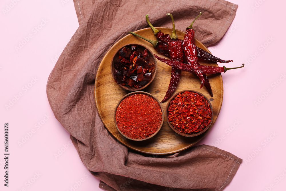 Plate with dry chili peppers and bowls of spices on pink background